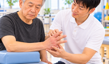 脳卒中後の手指の浮腫と疼痛を評価する理学療法士と高齢男性患者