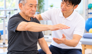 肩関節不安定症のリハビリで理学療法士が患者の肩甲骨を支えながら腕の挙上運動を指導する様子