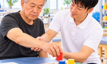 脳卒中患者がセラピストの介助を受けながら上肢のリーチ動作と物品把持を練習する様子